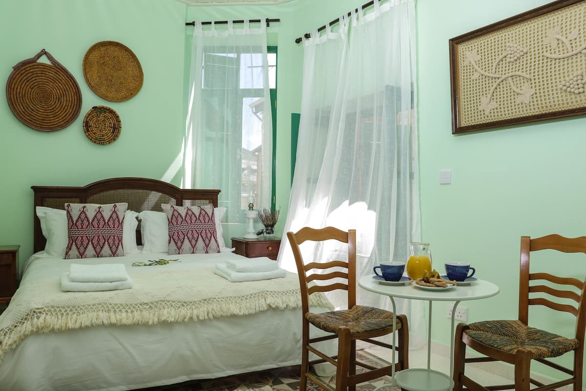 A neatly arranged bedroom with a bed, two chairs, a small table with breakfast items, and decorative wall hangings.