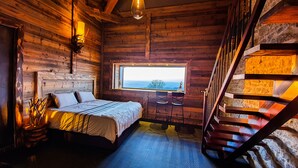 Un dormitorio de cabaña de madera con una cama, un ventanal con vistas y una escalera.