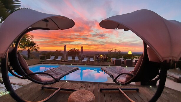 Zona de piscina con sillones de descanso y sombrillas, con vista a un atardecer.