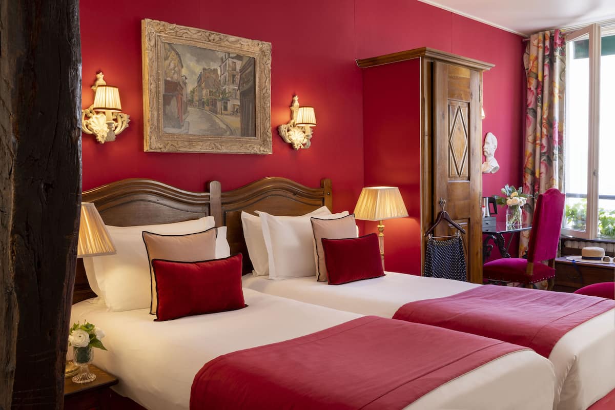 A hotel room with two beds, red walls, and a painting above the beds.