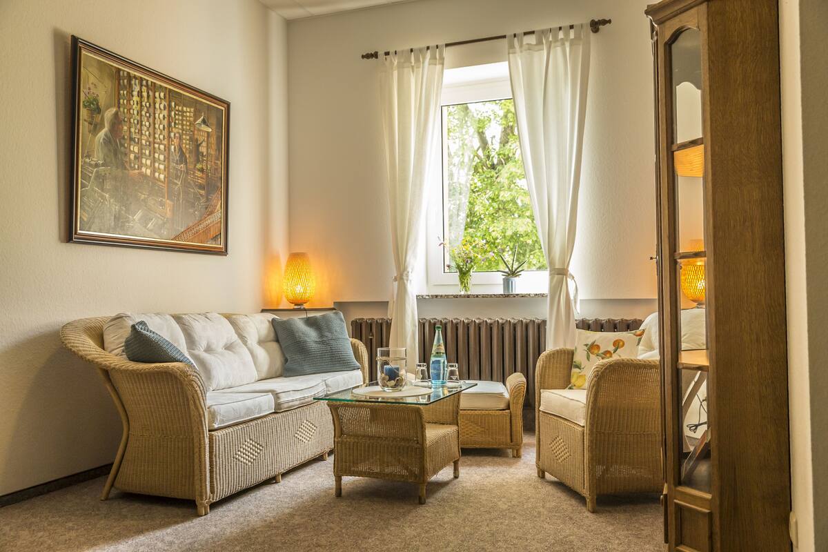 A cozy living room with a sofa, two armchairs, a glass coffee table, and a painting on the wall.