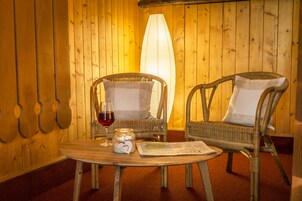 Um quarto aconchegante com duas cadeiras de vime, uma mesa de madeira, um candelabro de vidro e um copo de vinho tinto.