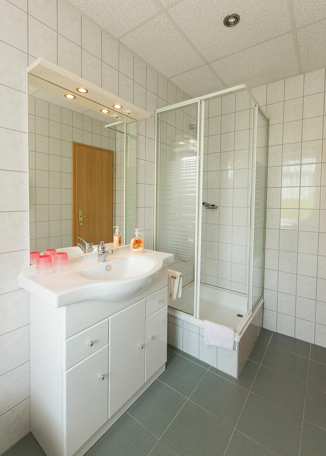 A modern bathroom with a white sink, mirror, and glass shower enclosure.