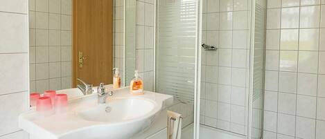 A modern bathroom with a white sink, mirror, and glass shower enclosure.