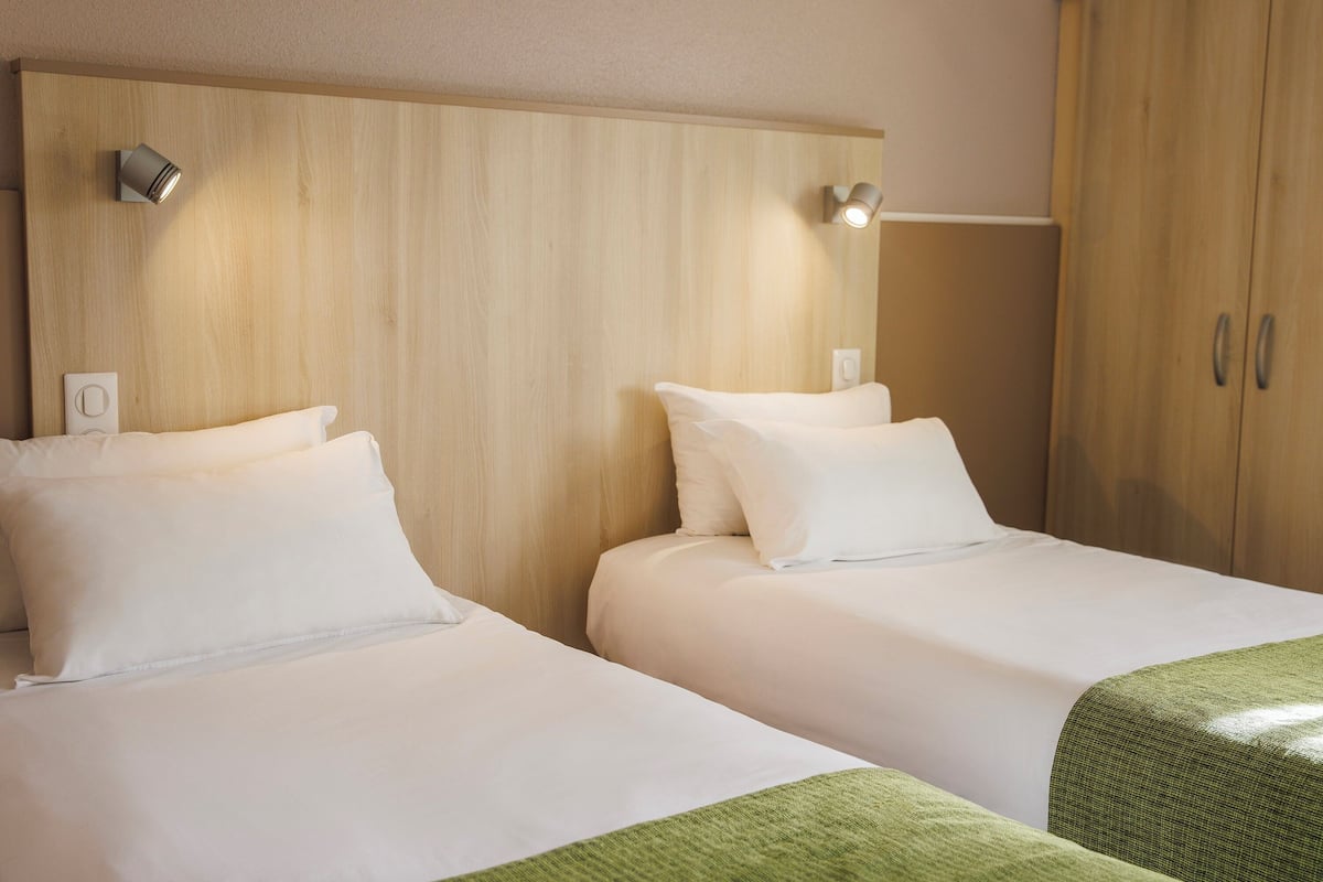 A hotel room with two beds, wooden headboard, and a wardrobe.