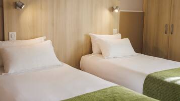 Quarto de hotel com duas camas, cabeceira de madeira e um guarda-roupa.