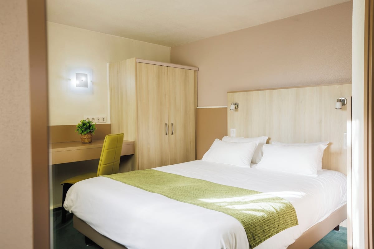A hotel room with a bed, a desk, a chair, and a wardrobe.