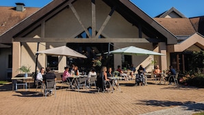 An outdoor patio area with tables and chairs, a covered seating area, and a building with a pitched roof and large windows. - Hotel Mont Vernon (Saint-Marcel)
