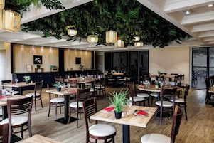 Un restaurante con mesas y sillas de madera, plantas colgantes e iluminación colgante.