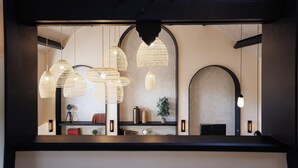 A reception area with hanging woven light fixtures, a plant, and a shelf with books and decorative items. - Hotel Mont Vernon (Saint-Marcel)