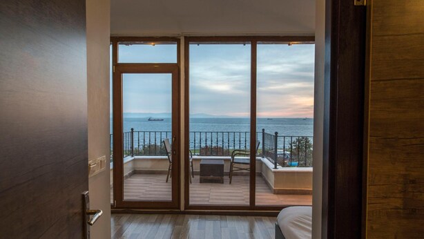 A room with a large sliding glass door leading to a balcony with a view of the sea and a ship in the distance. - Bucoleon Hostel (Istanbul)