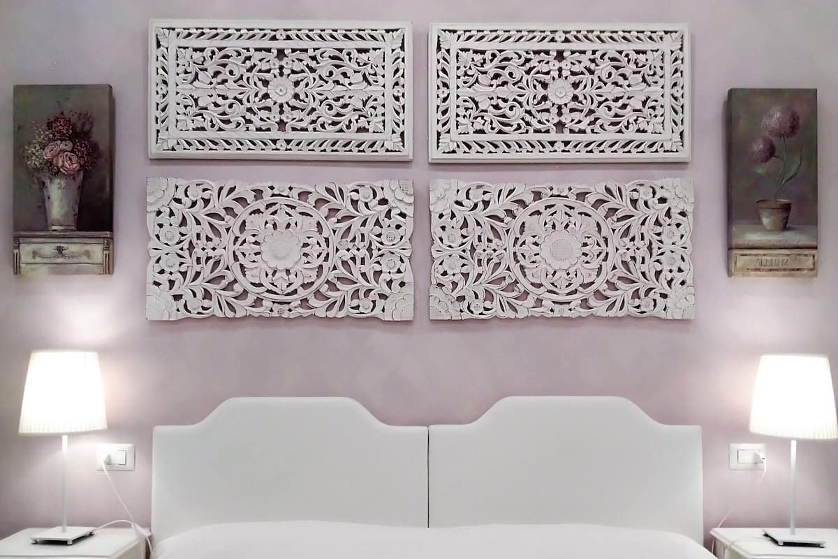 Une chambre à coucher avec un lit blanc, deux tables de chevet avec des lampes et quatre panneaux décoratifs fixés au mur.