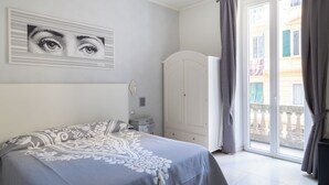 A bedroom with a bed, a white wardrobe, a door, and a view of a building through a window. - Golfo Della Luna (La Spezia)