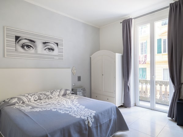 A bedroom with a bed, a white wardrobe, a door, and a view of a building through a window.