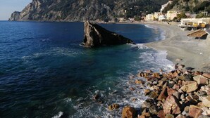 A rocky beach with a prominent rock formation in the water, a sandy shore, and buildings in the background. - Golfo Della Luna (La Spezia)
