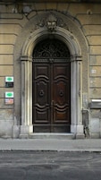 Una puerta doble de madera con un arco decorativo, ubicada en un edificio de piedra.