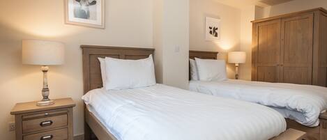 Une chambre d’hôtel avec deux lits simples, une table de chevet en bois avec une lampe et une armoire.