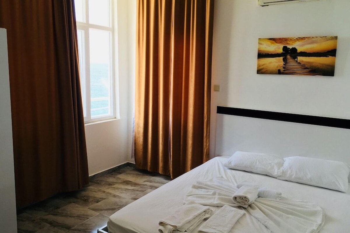 A hotel room with a bed, curtains, a painting, and a window.