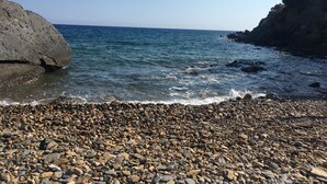 A rocky beach with clear blue water and a large rock formation on the left. - Pinar Motel 2022-33-0198 (Aydincik)