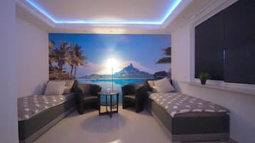 Een kamer met een strandfries, twee banken, een kleine tafel en een raam met zonwering.