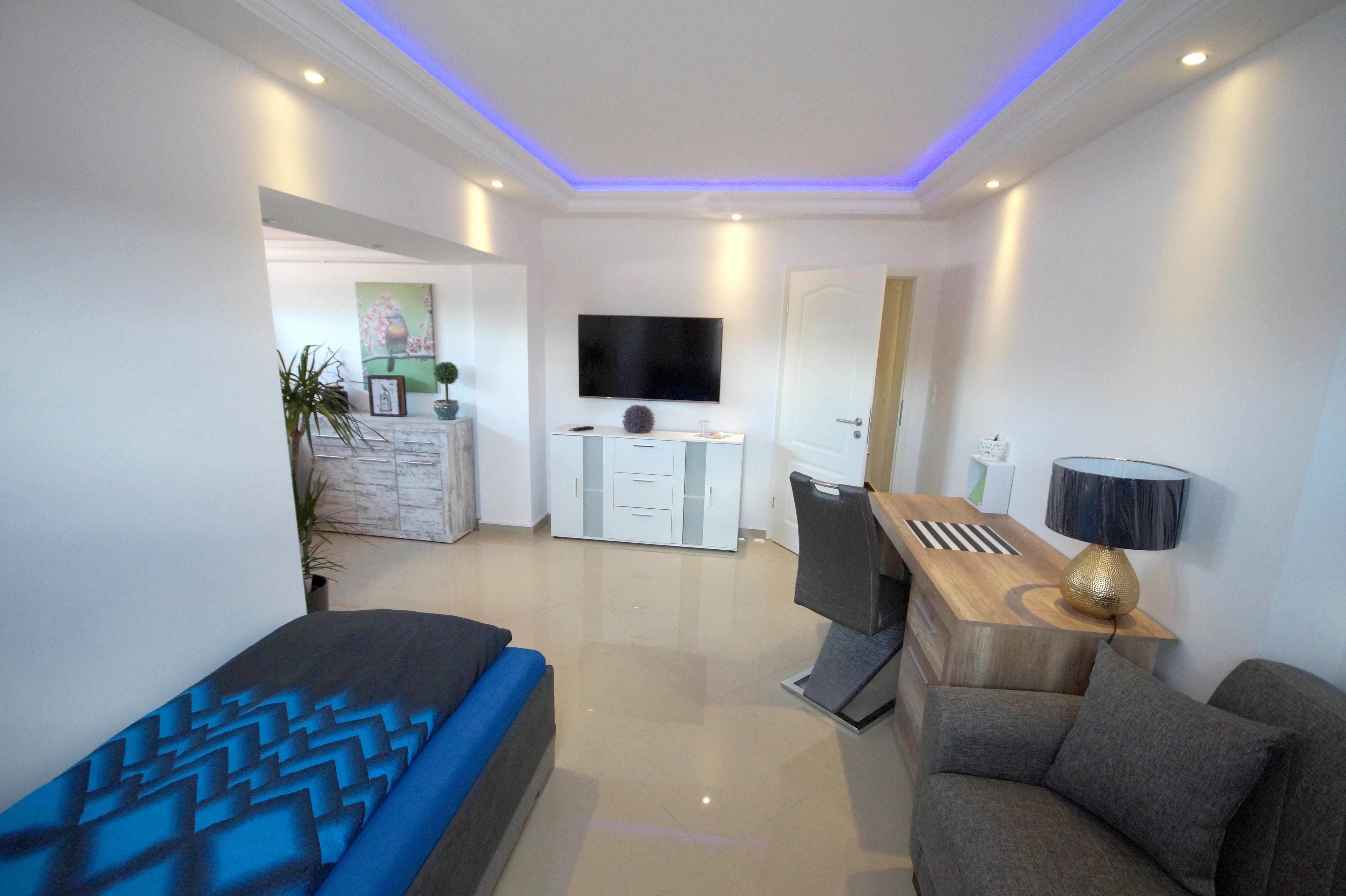 Un dormitorio moderno con cama, escritorio, silla, televisor y lámpara.
