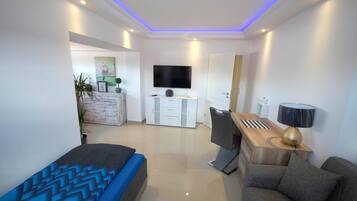 Un dormitorio moderno con cama, escritorio, silla, televisor y lámpara.