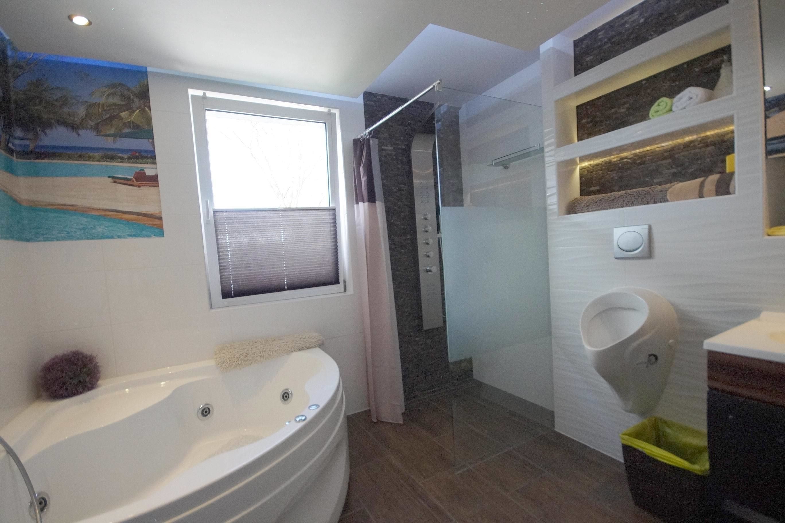 A modern bathroom with a large bathtub, a glass shower enclosure, a toilet, and a built-in shelf with towels.