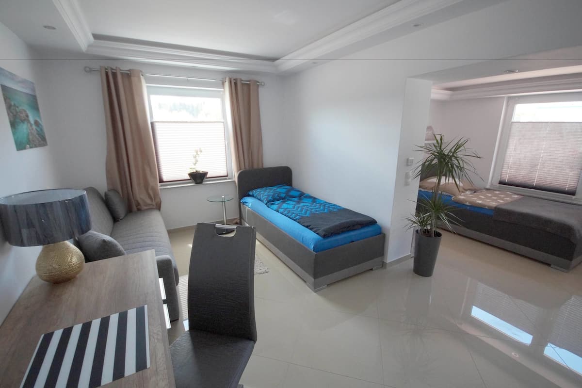 Quarto moderno com cama, sofá, escrivaninha e janela com cortinas.