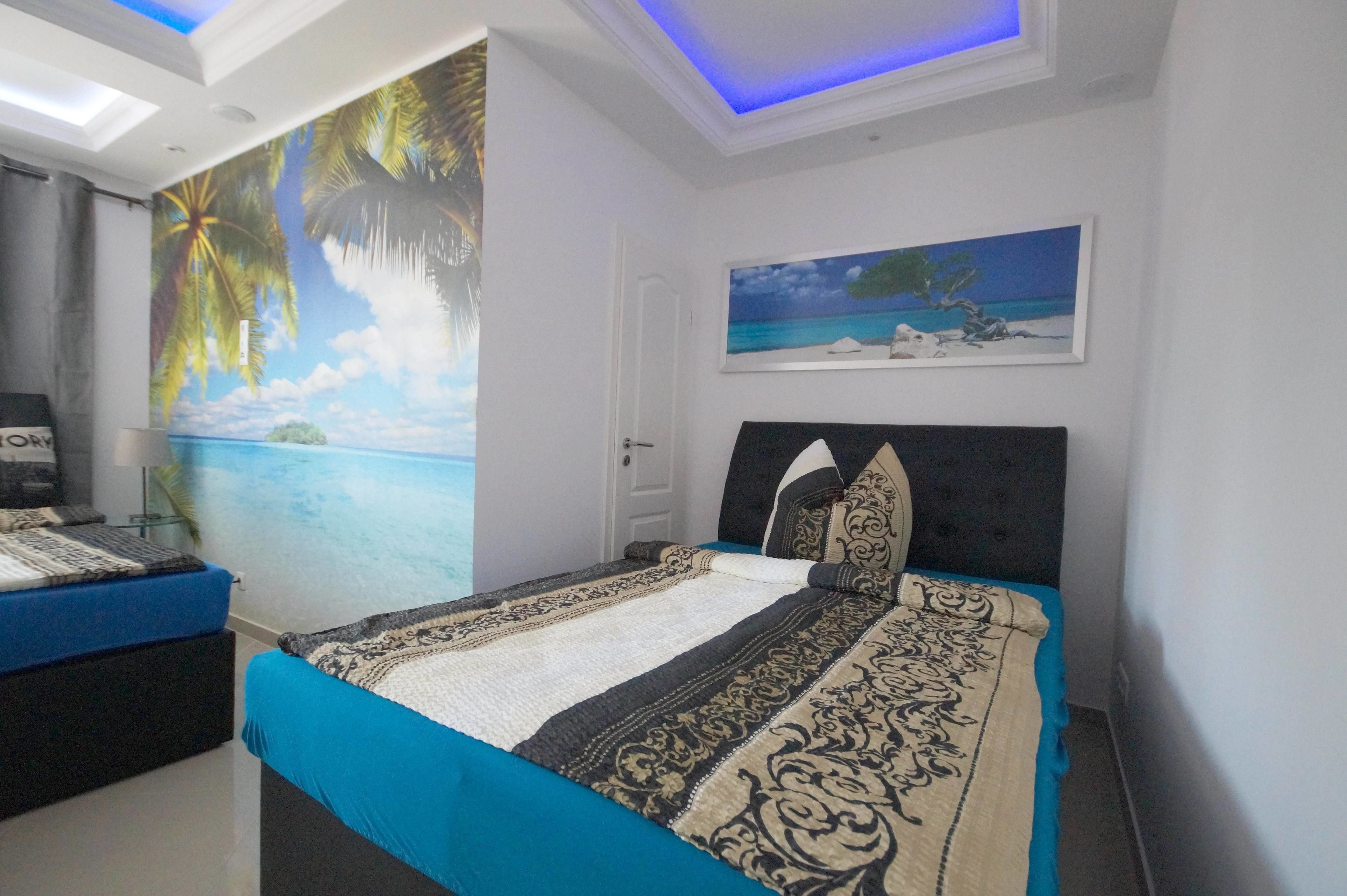 A bedroom with a bed, a nightstand, a painting, and a mural of a beach scene.