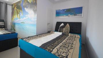 A bedroom with a bed, a nightstand, a painting, and a mural of a beach scene.