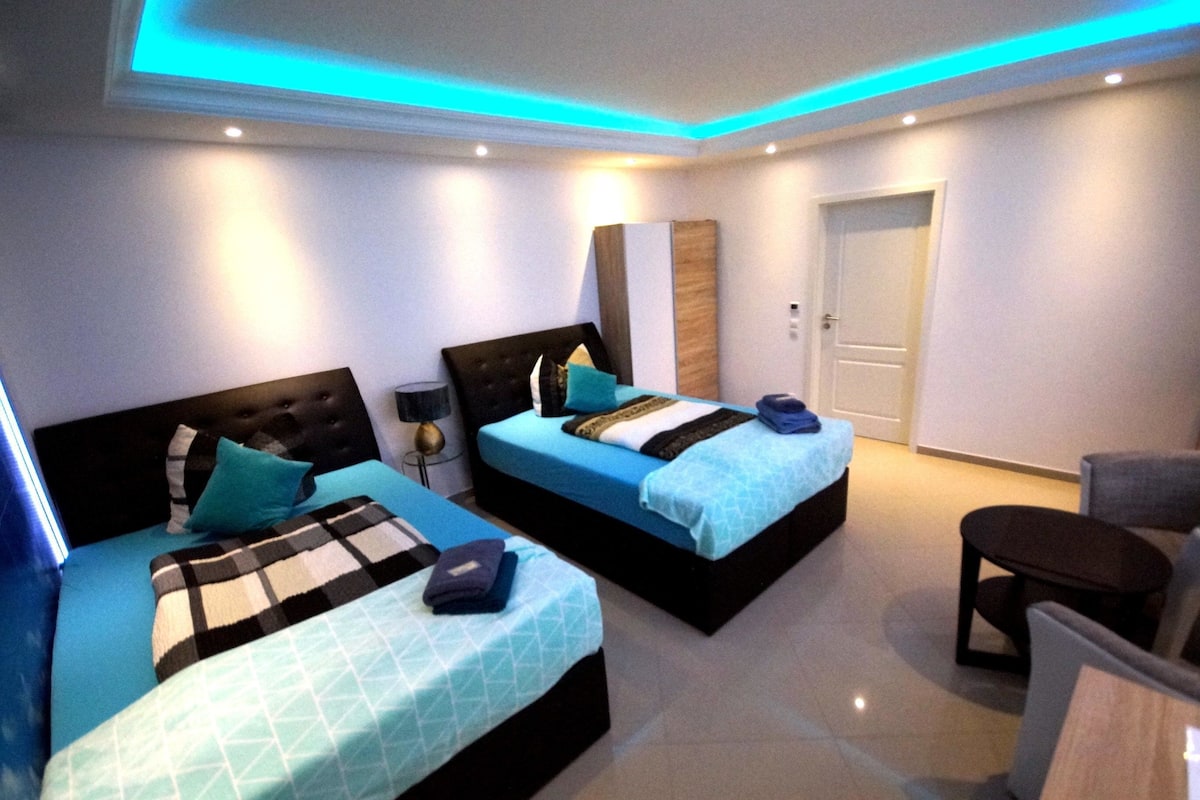 Quarto de hotel moderno com duas camas, uma mesa pequena e uma cadeira.