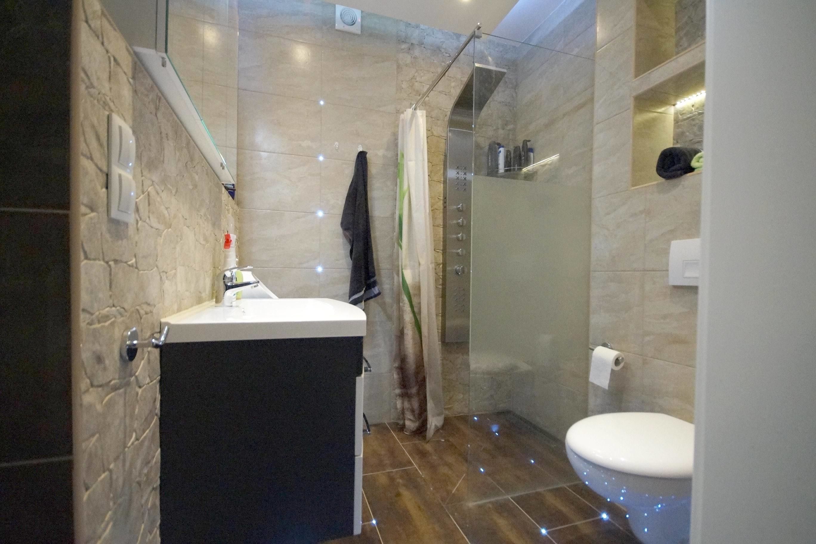 Un bagno moderno con parete in pietra, box doccia in vetro, servizi igienici bianchi e lavabo con specchio.