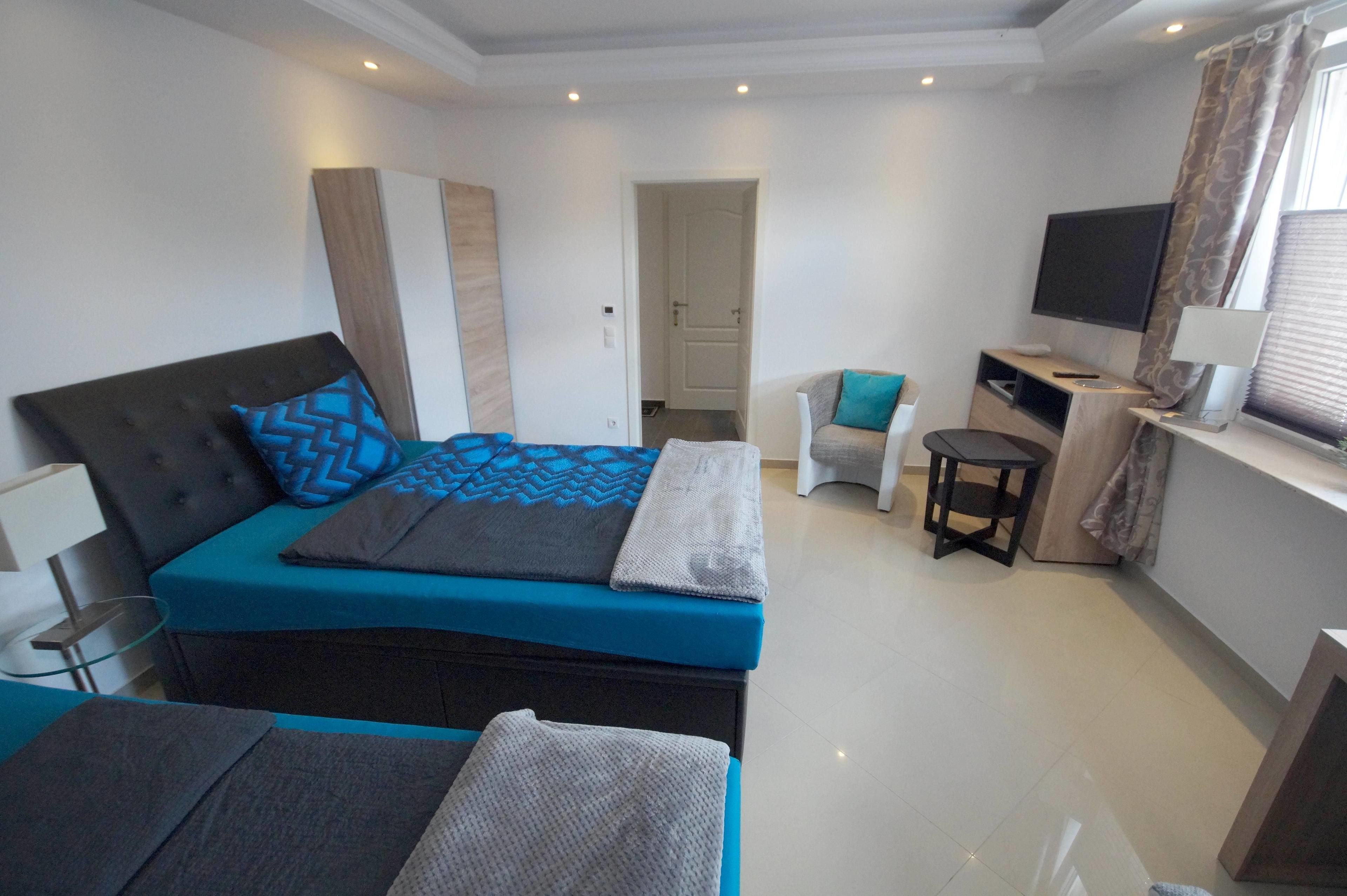 Quarto moderno com uma cama grande, um espaço de descanso pequeno e uma televisão.