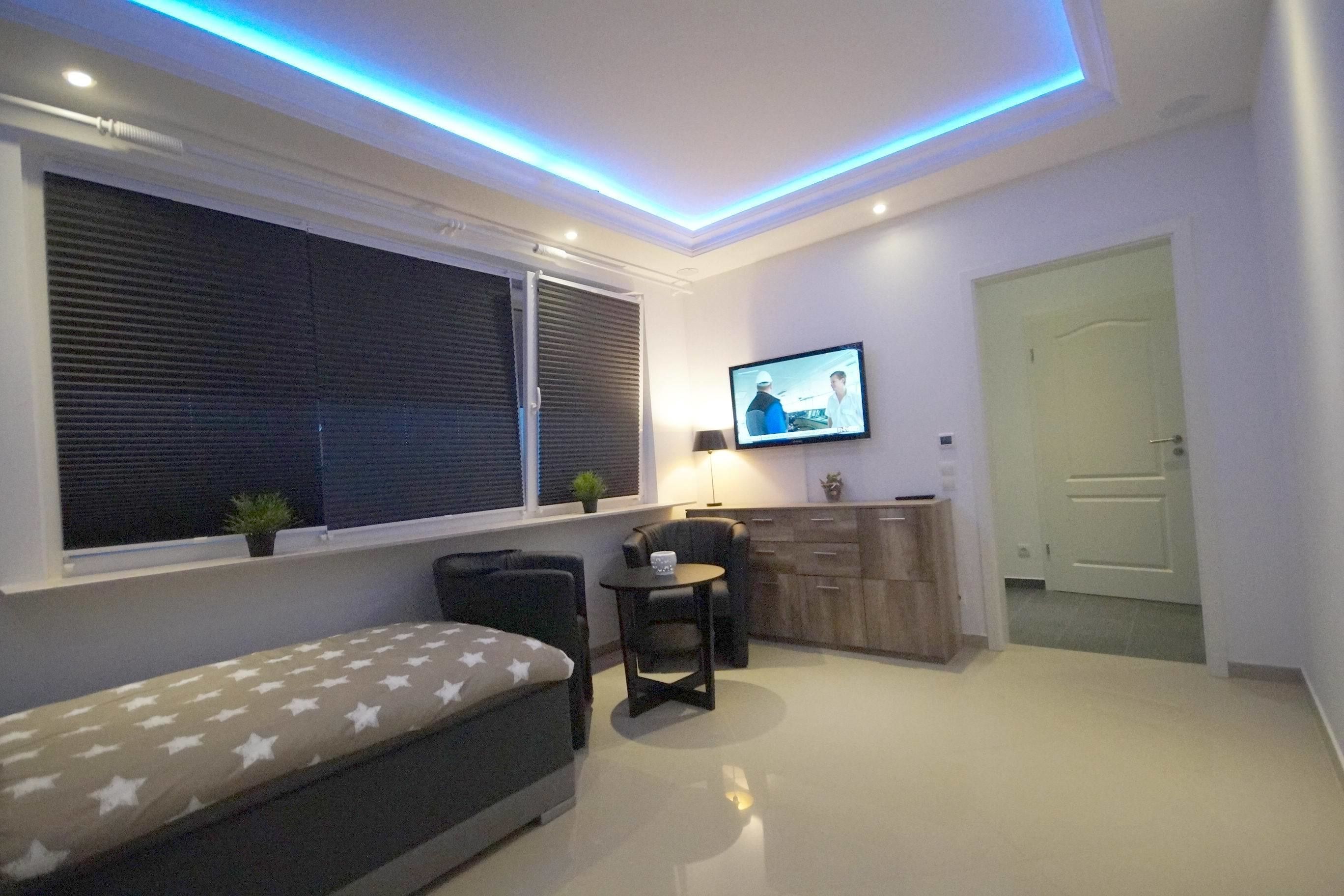 A modern bedroom with a bed, a small table, a TV, and a window with blinds.