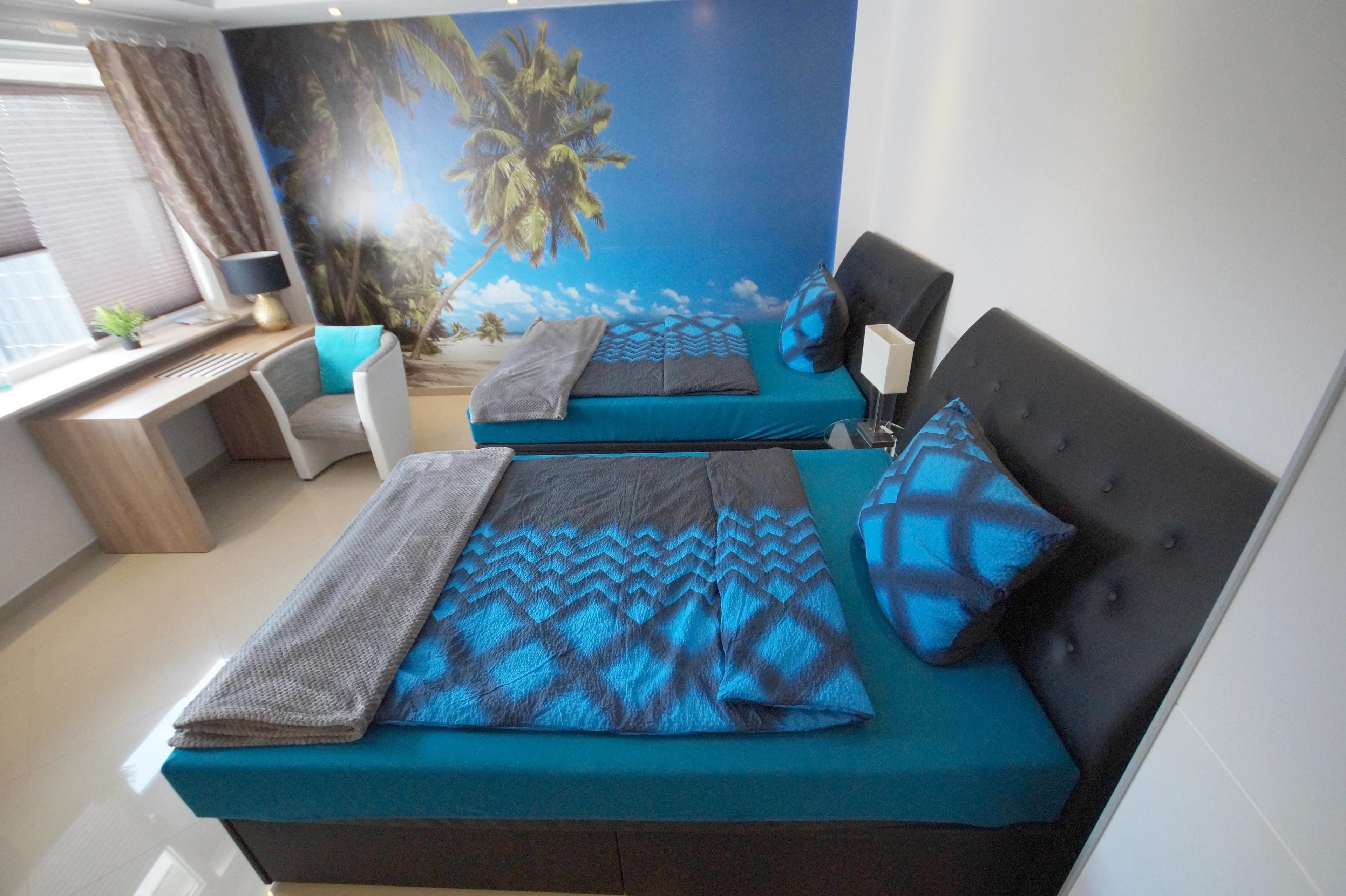Ein Zimmer mit zwei Betten, einem Schreibtisch und einer großen Wandmalerei im tropischen Stil.