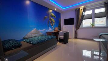 A modern bedroom with a mural of a tropical scene, a bed with patterned pillows, a desk, and a window with curtains.