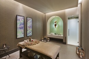 A spa room with a massage table, artwork, a green-lit arch, and a shower area.