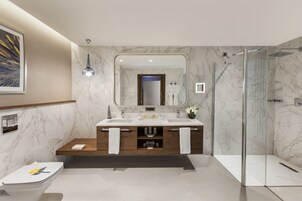 A modern bathroom with a marble backsplash, a double sink vanity, a glass shower enclosure, and a framed artwork on the wall.