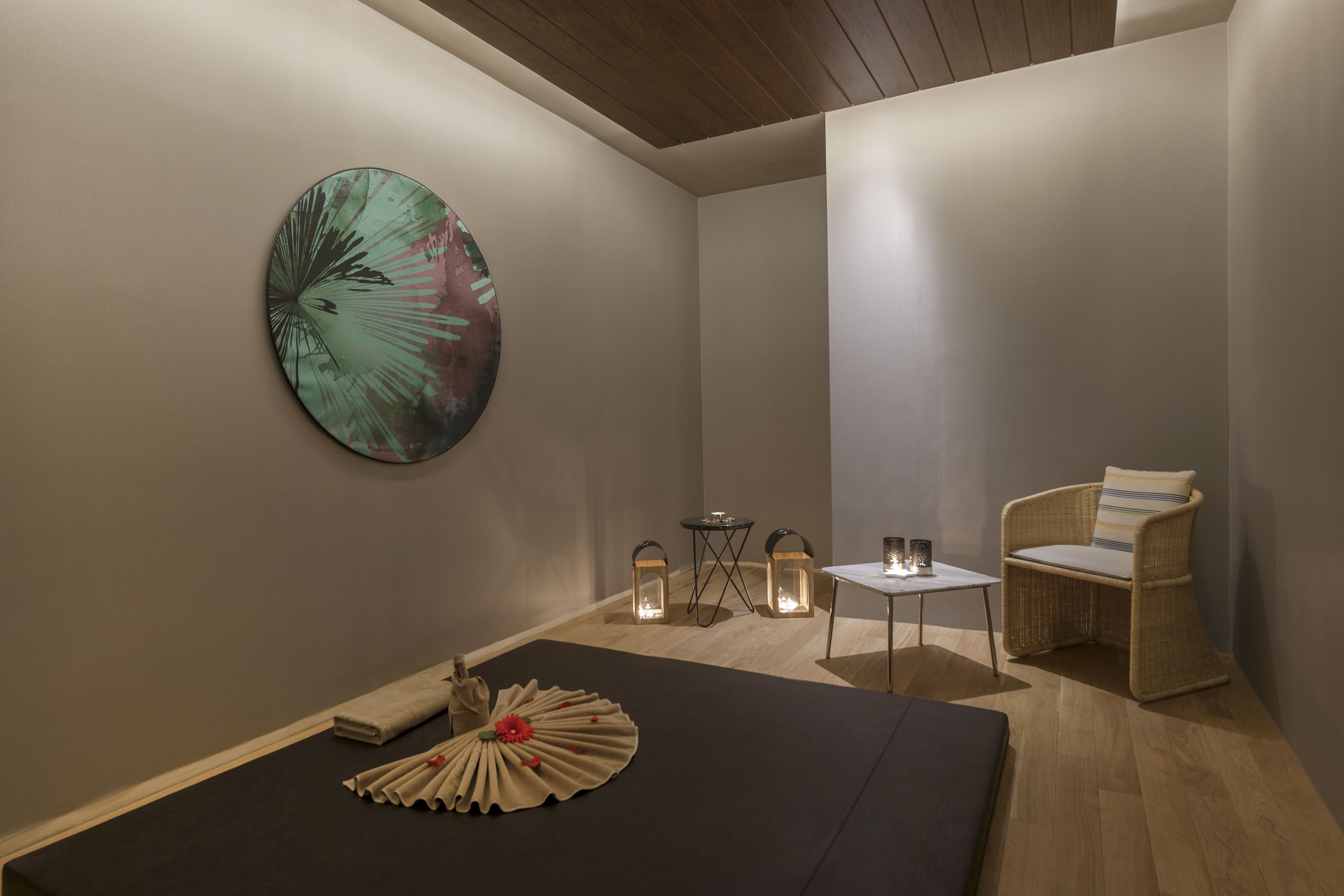 A minimalist room with a bed, a chair, a small table, and a wall-mounted artwork.