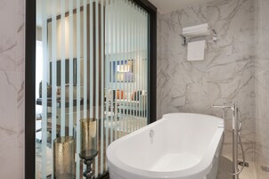 A modern bathroom with a freestanding bathtub, a glass partition, and marble walls.