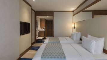 Habitación de hotel con dos camas, televisión, escritorio y baño visible a través de una puerta abierta.