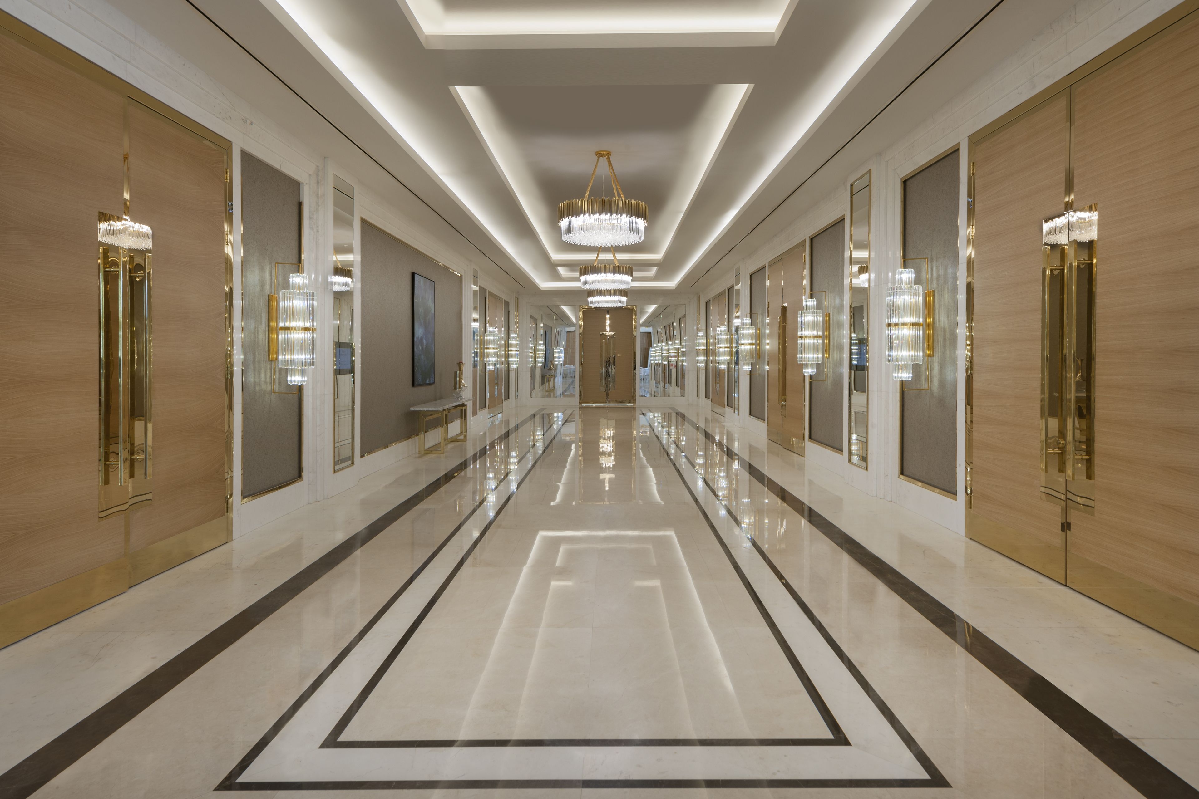 A long, well-lit hallway with reflective floors, large chandeliers, and mirrored walls.
