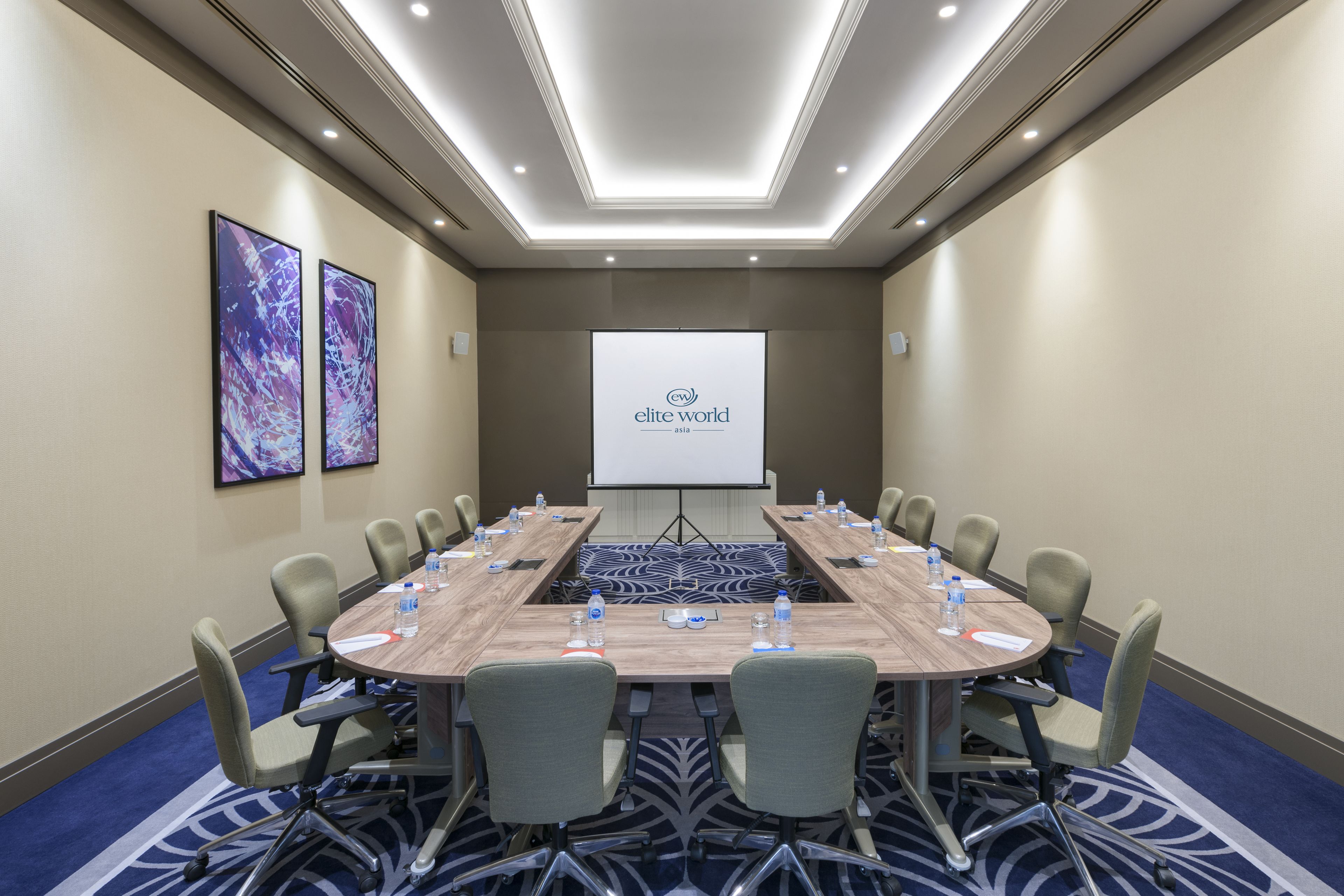 A conference room with a long table, chairs, and a projector screen displaying "elite world asia".