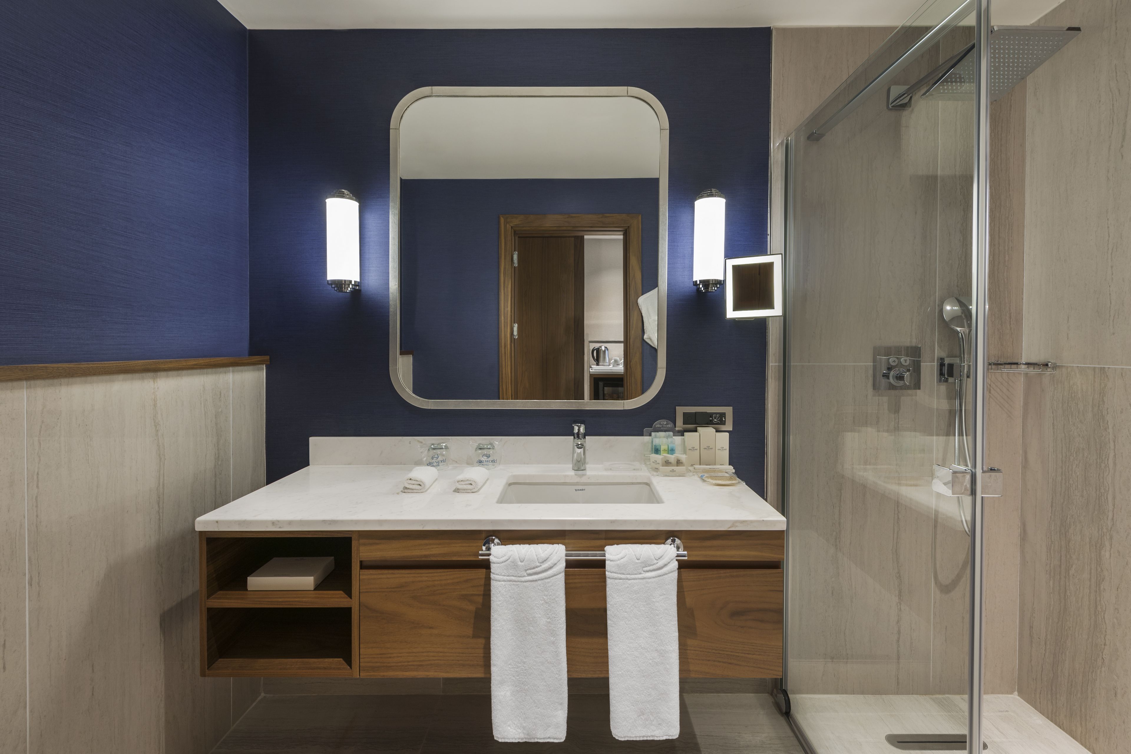 A modern bathroom with a large mirror, white sink, and a glass-enclosed shower.