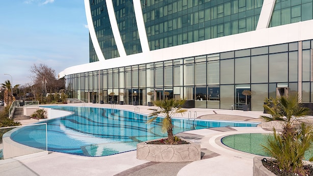 A modern hotel with a large pool area, featuring a curved pool design and a large glass facade. - Elite World Grand Istanbul Kucukyali  (Istanbul)
