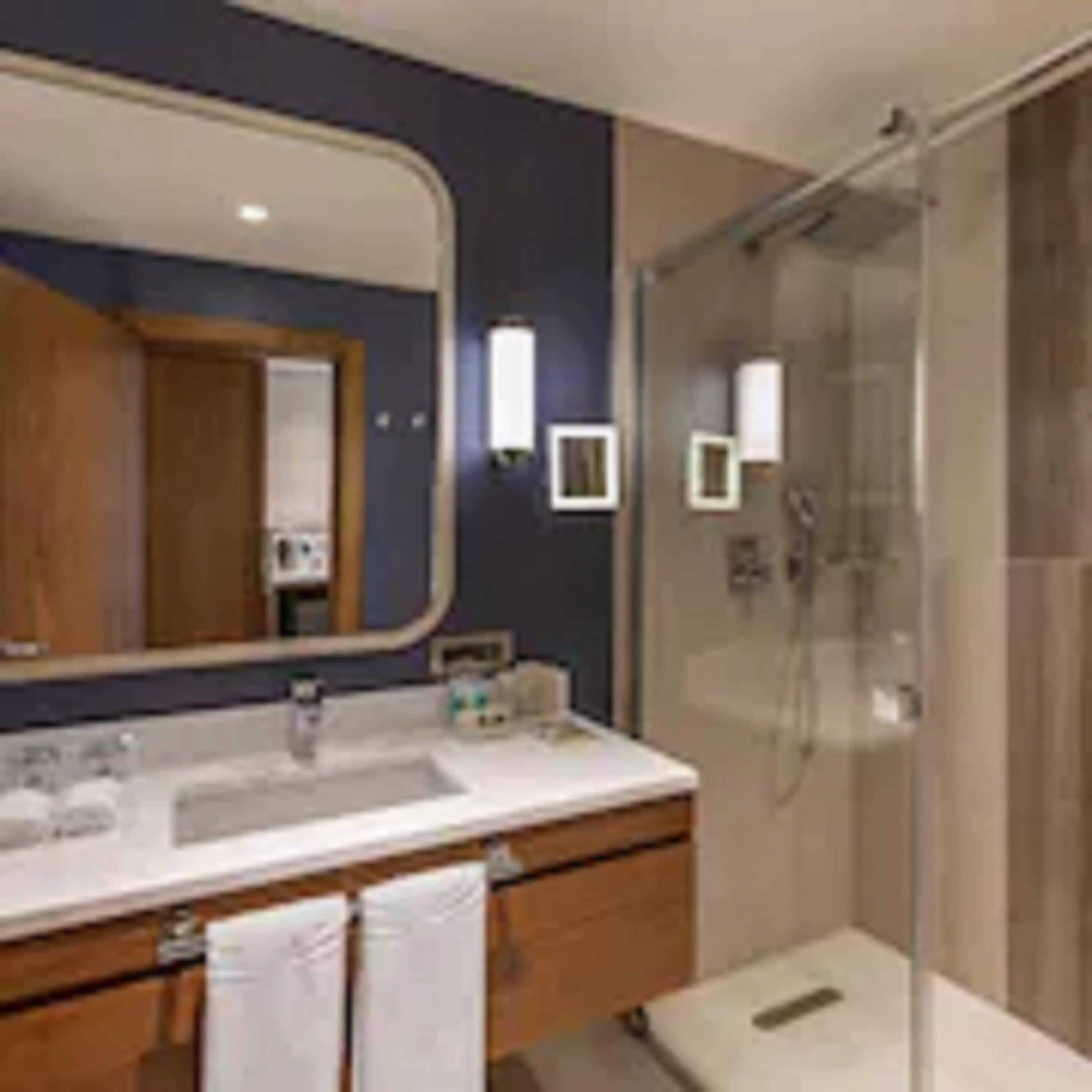 Une salle de bain moderne avec un grand miroir, une douche et un meuble-lavabo doté d’un évier et d’un porte-serviettes.