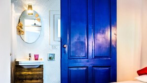 A room with a blue door, a white sink with a mirror, and a wooden cabinet. - B&B la di Cesar (Aiello del Friuli)
