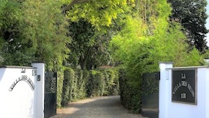 Ein begrenzter Zugang zur Villa Des Sens, ein Kiesweg führt durch dichtes Grün.
