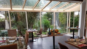Ein moderner Essbereich mit Innenarchitektur, Glaswänden, Korbstühlen und einem Tisch, gedeckt mit Tellern, Tassen und einer Obstschale.