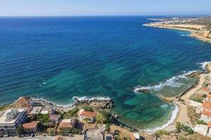A coastal town with clear blue waters, rocky shoreline, and buildings with red-tiled roofs. - Astrantia-Adults Only (Chania)